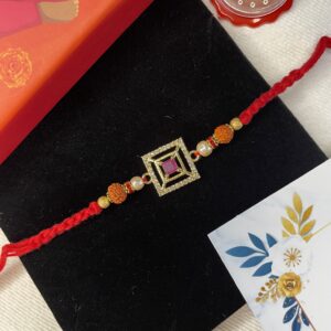 Red Stone Golden Rakhi with Chandan Tika, Handkerchief, Personalized Card & Eco-Friendly Gift Box