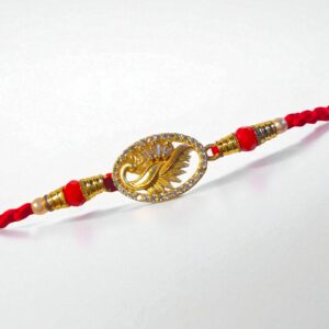 Golden swan-themed rakhi with crystal-studded border on a red thread, placed on a white background.